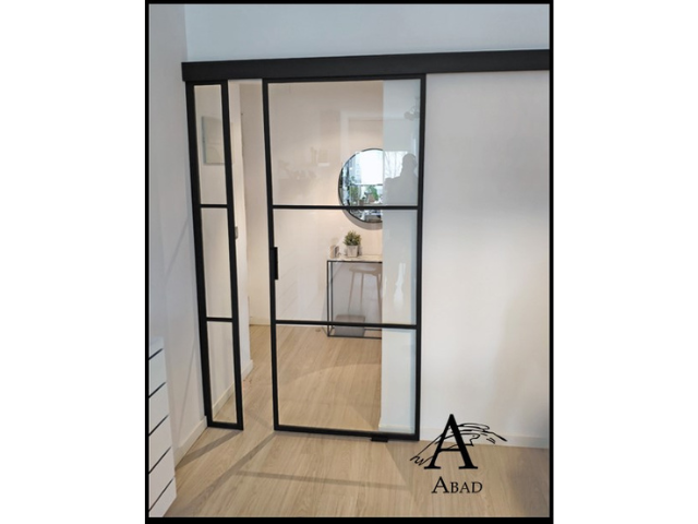 Puerta de forja acristalada con un lado fijo y una hoja corredera.